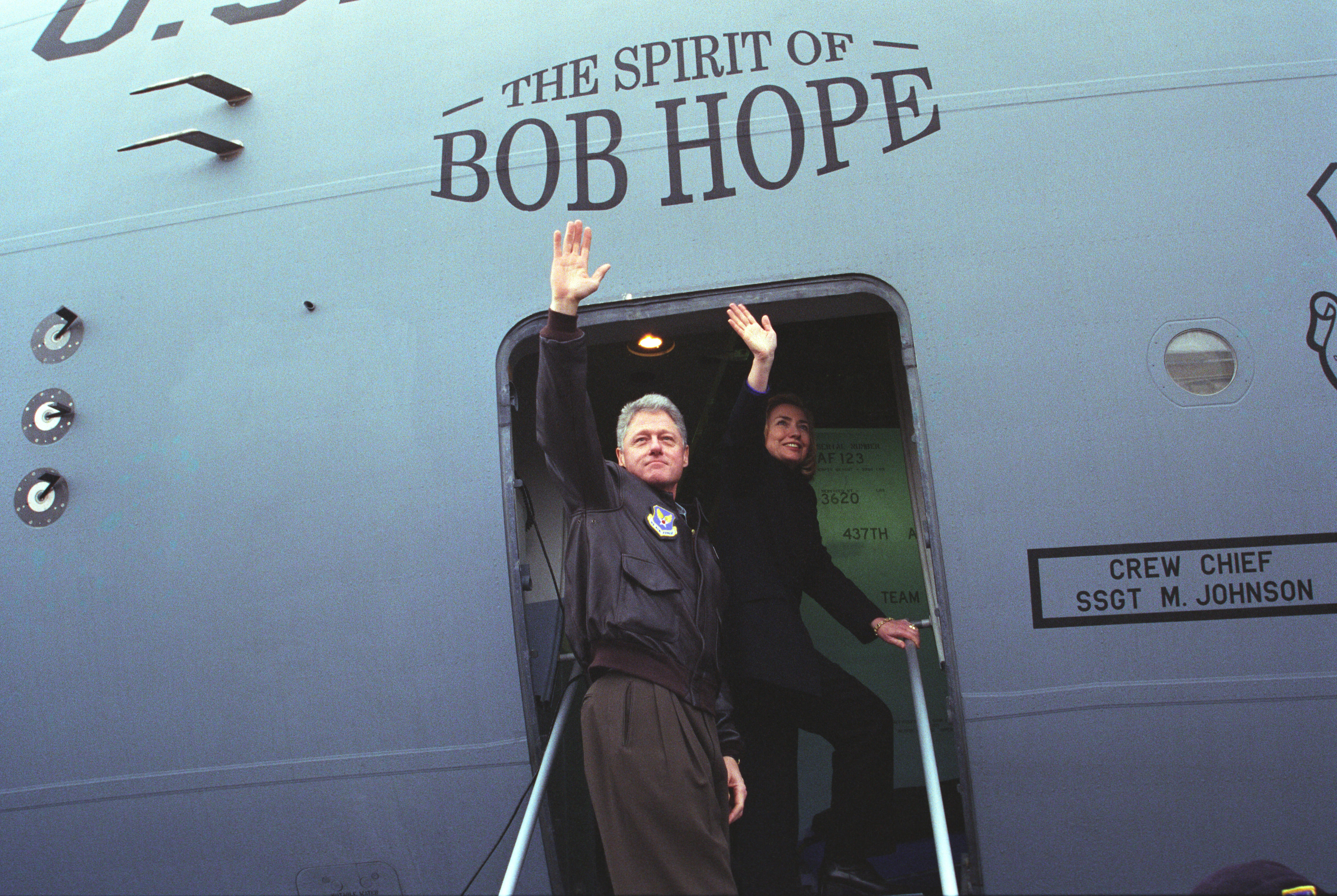 President Clinton, and First Lady Hillary Rodham Clinton wave from the doorway of "The Spirit of Bob Hope" airplane in Sarajevo, Bosnia-Herzegovina