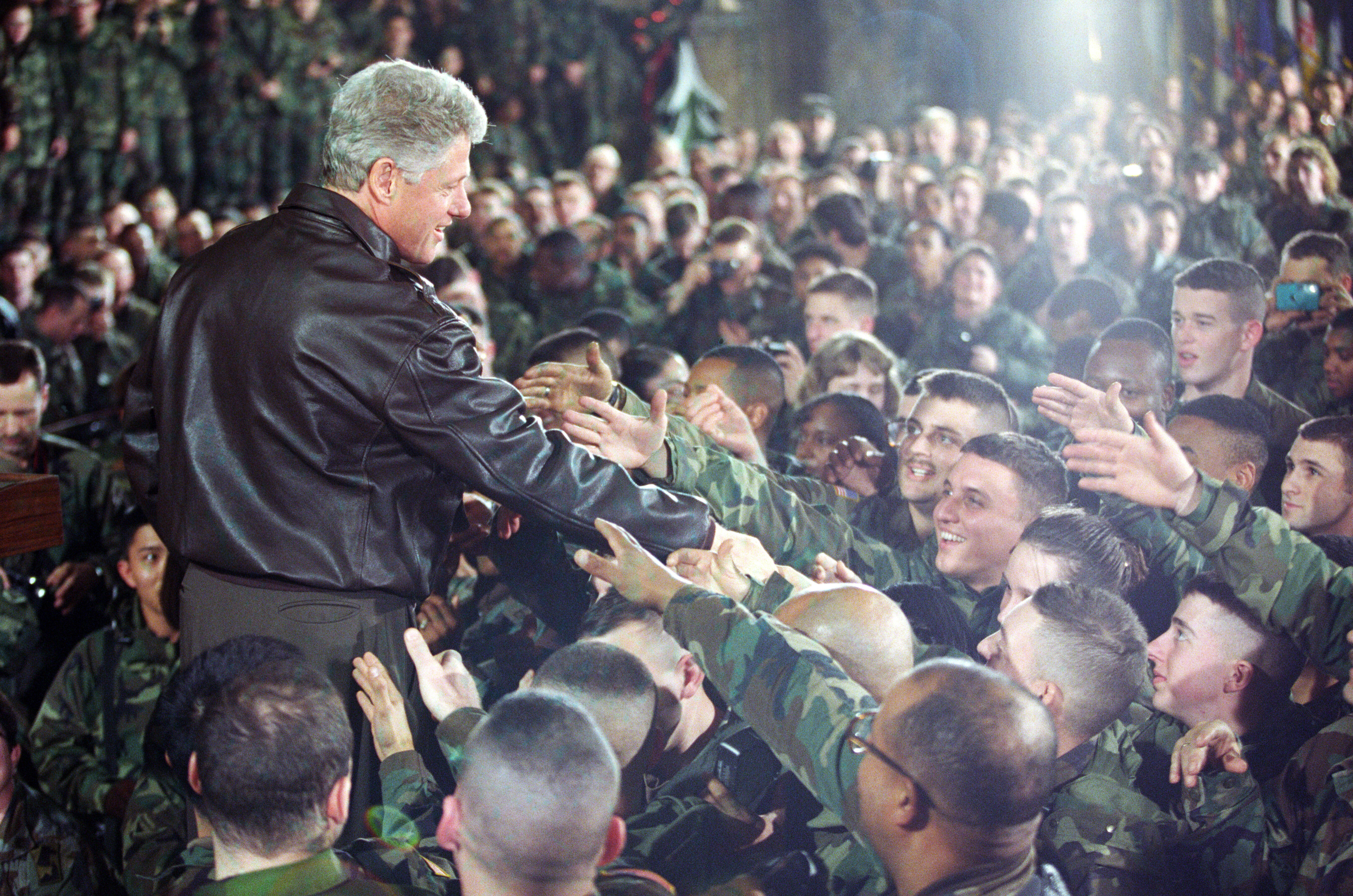 President Clinton stands elevated, looking down at the troops. The Troops look up reaching their hands toward President Clinton. President Clinton greets troops during his visit to Tuzla Air Force Base in Bosnia-Herzegovina.