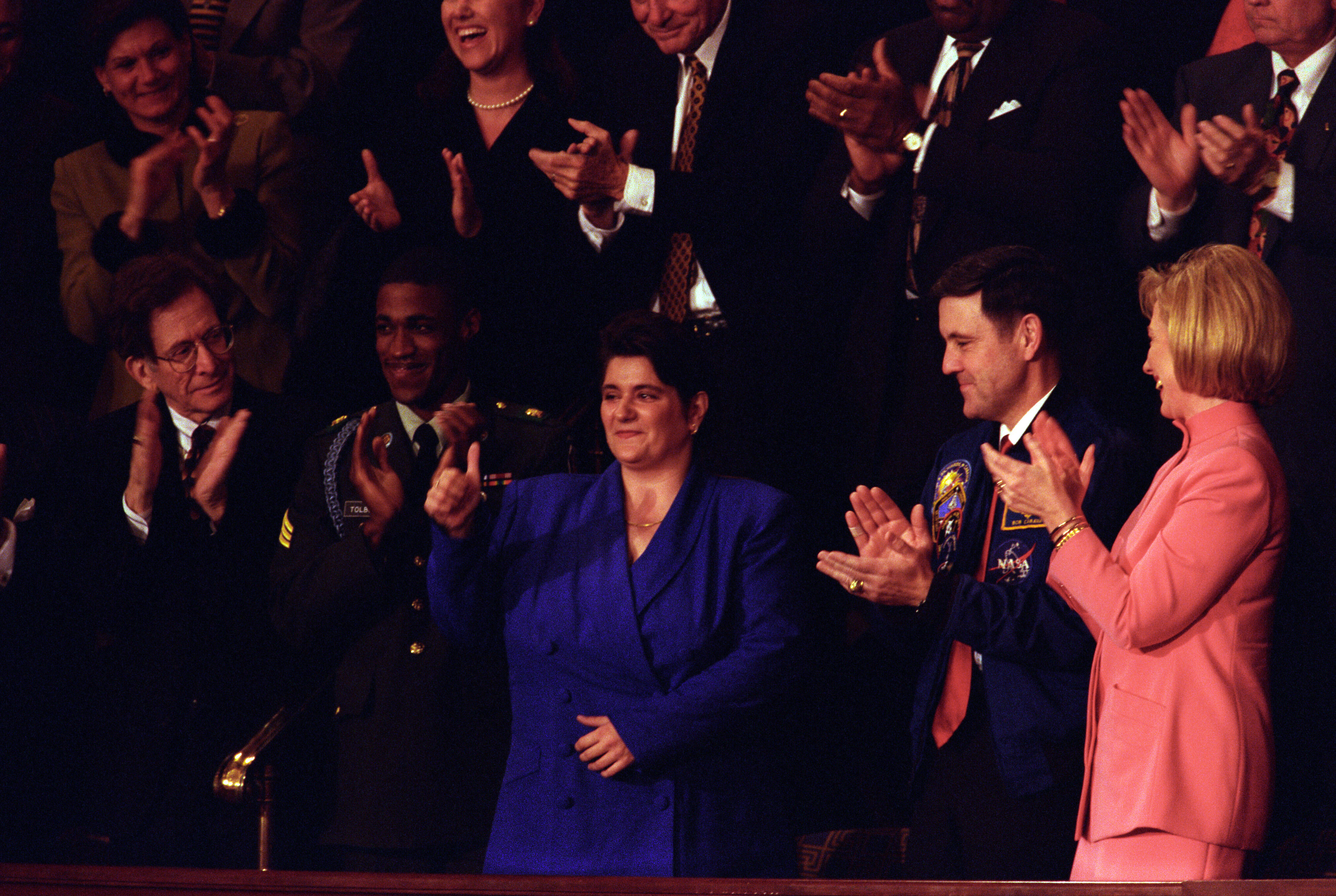 First Lady Hillary Rodham Clinton attends the State of the Union in the House Chamber at the United States Capitol, Washington D.C. She is seated in the visitors gallery with former welfare recipient Elaine Kinslow and Army Sergeant Michael Tolbert who served in Bosnia. The President acknowledges Kinslow and Tolbert