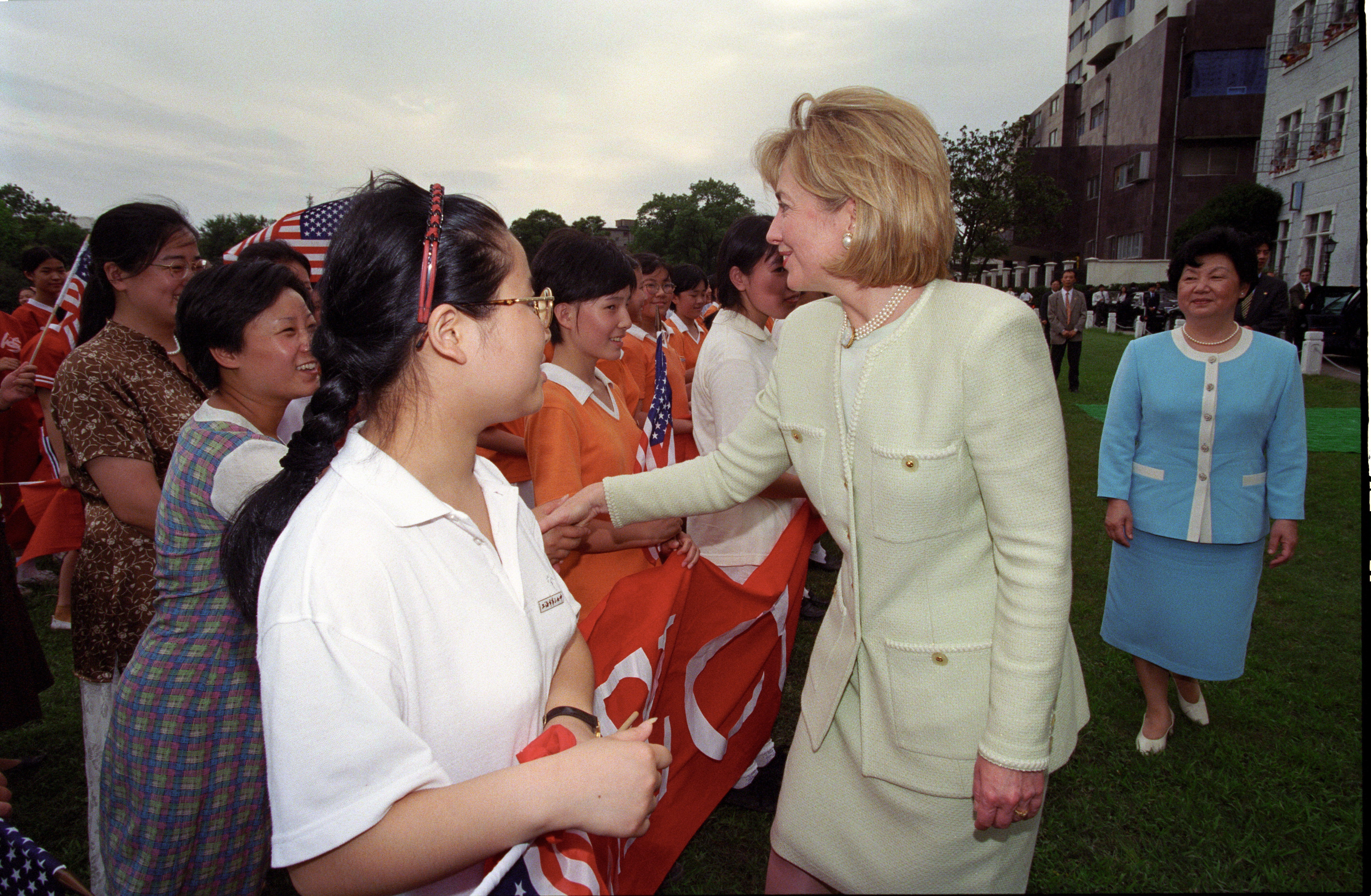 Hillary Rodham Clinton shakes hands with girls from the Shanghai No. 3 Girls School in Shanghai, China. The Girls hold a sign that reads, "First Lady of the United States of America"