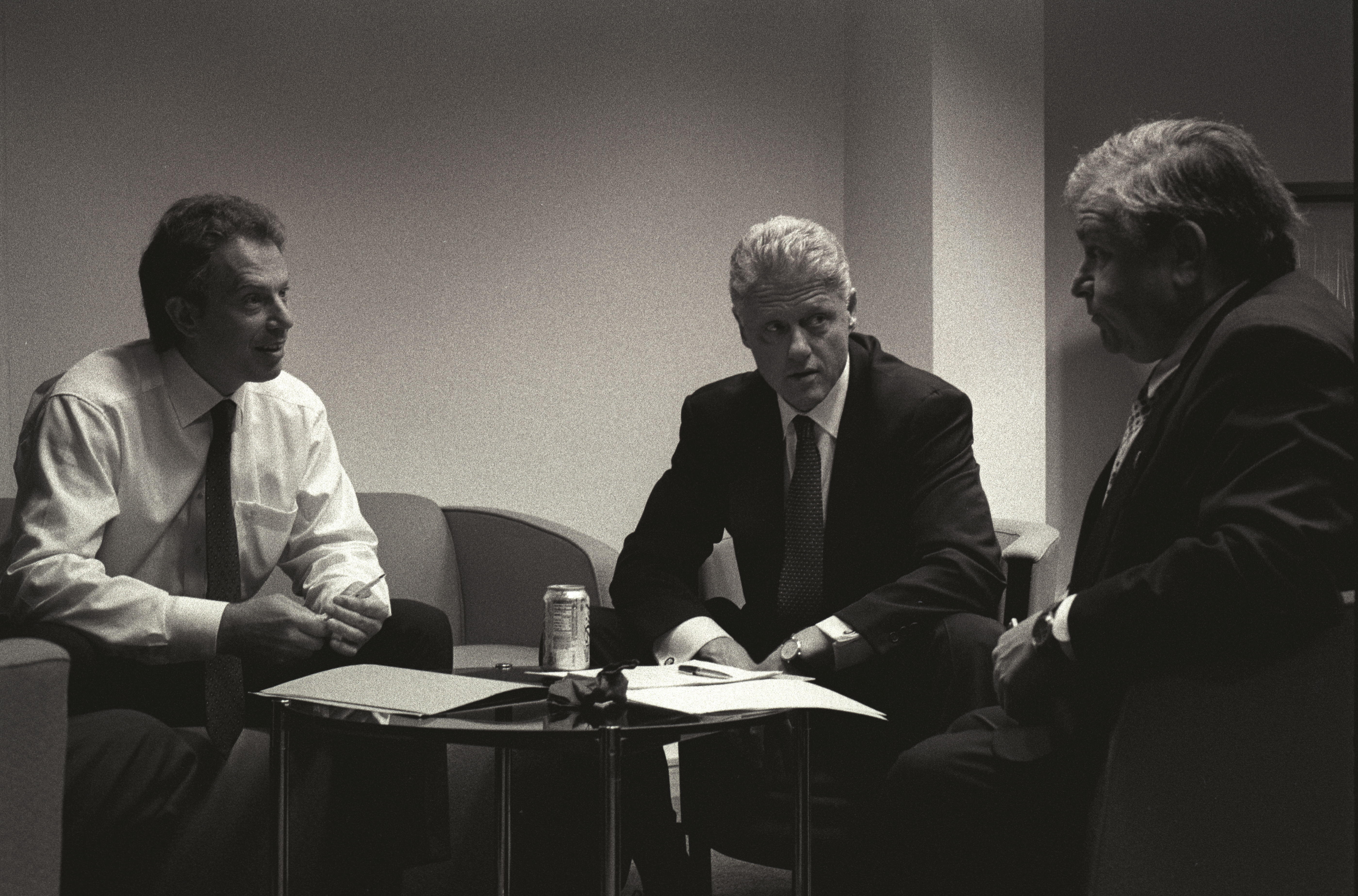 Black and white photograph. President Clinton sits and talks with Prime Minister Tony Blair and Sandy Berger