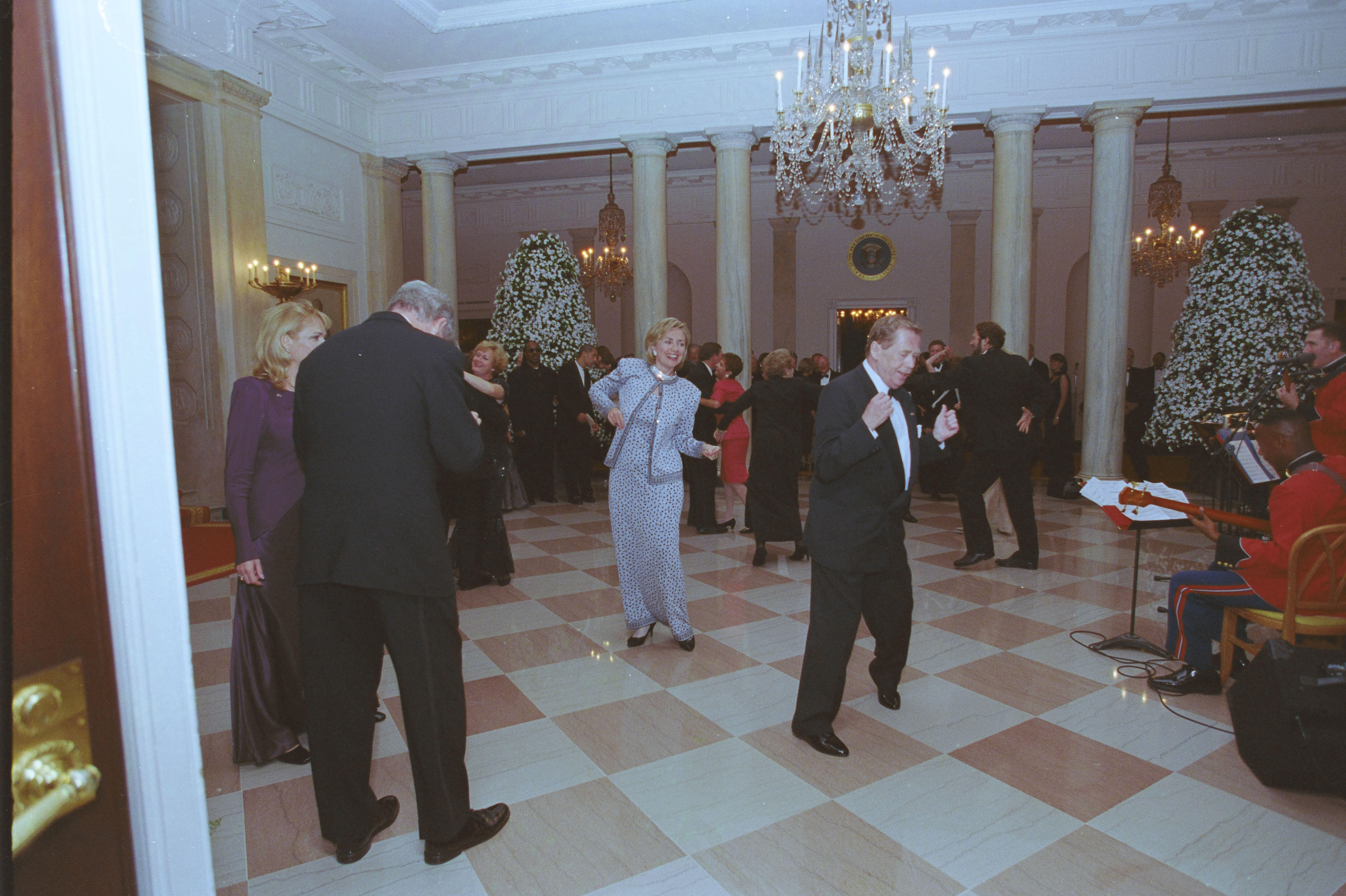 First Lady Hillary Rodham Clinton and President Václav Havel dance together. President Clinton stands next Dagmar Havlová. President Clinton holds his head down. 