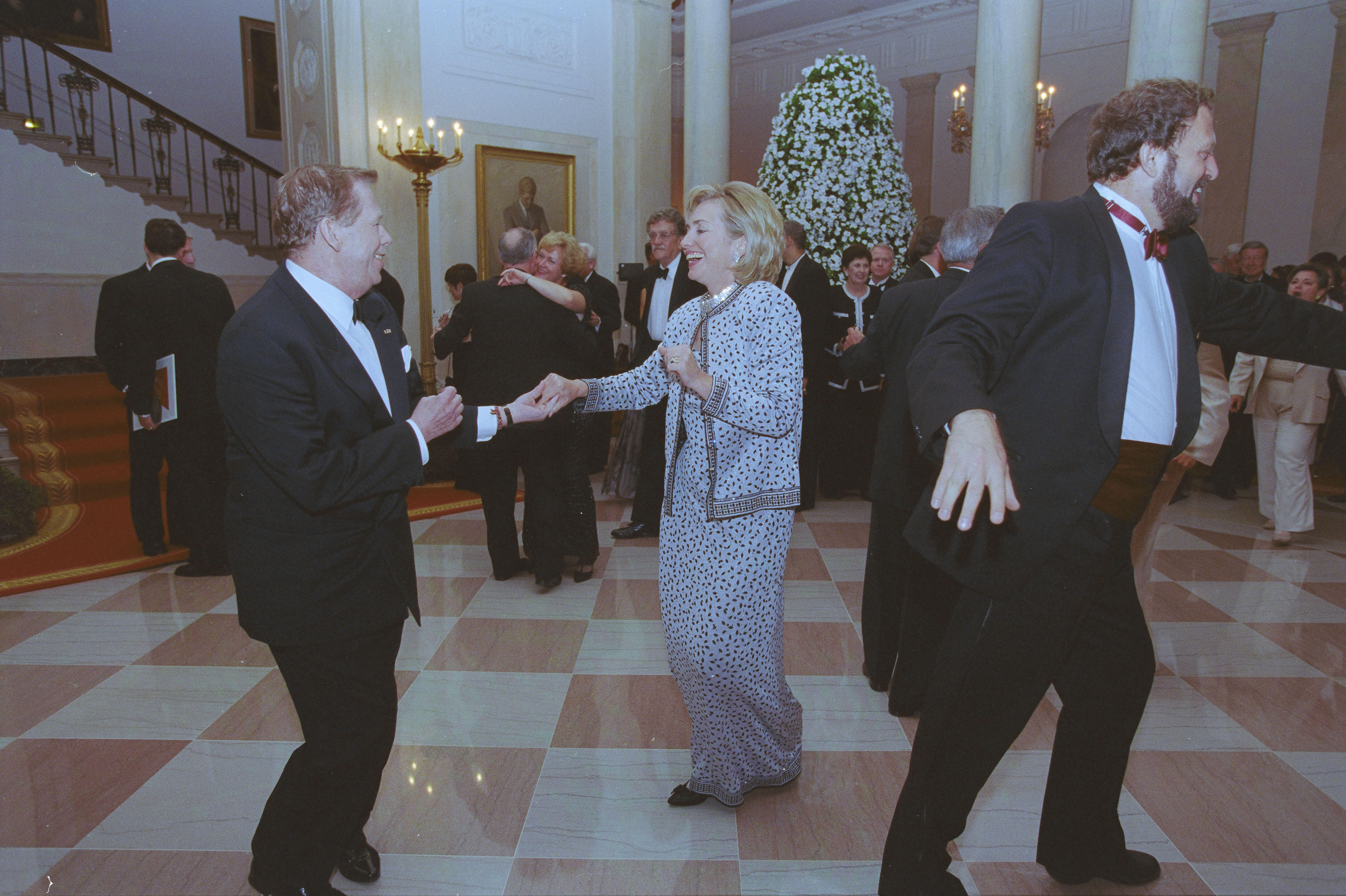 First Lady Hillary Rodham Clinton and President Václav Havel dance holding hands. Other dinner attendees dance in the background.