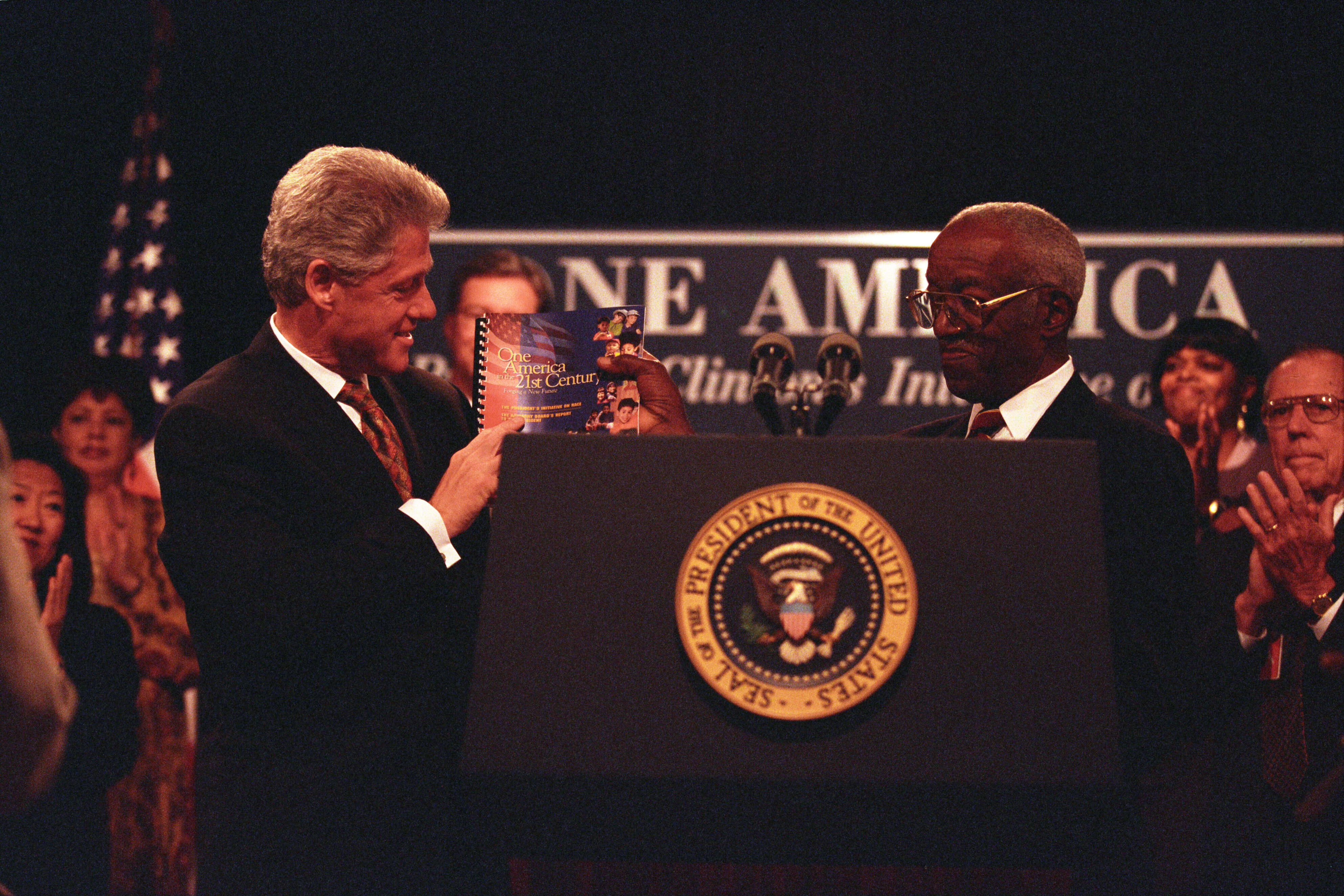 President Clinton holds up a report titled 'One America 21st Century' with historian, John Hope Franklin, at an event where the President addresses the President's Advisory Board on Race