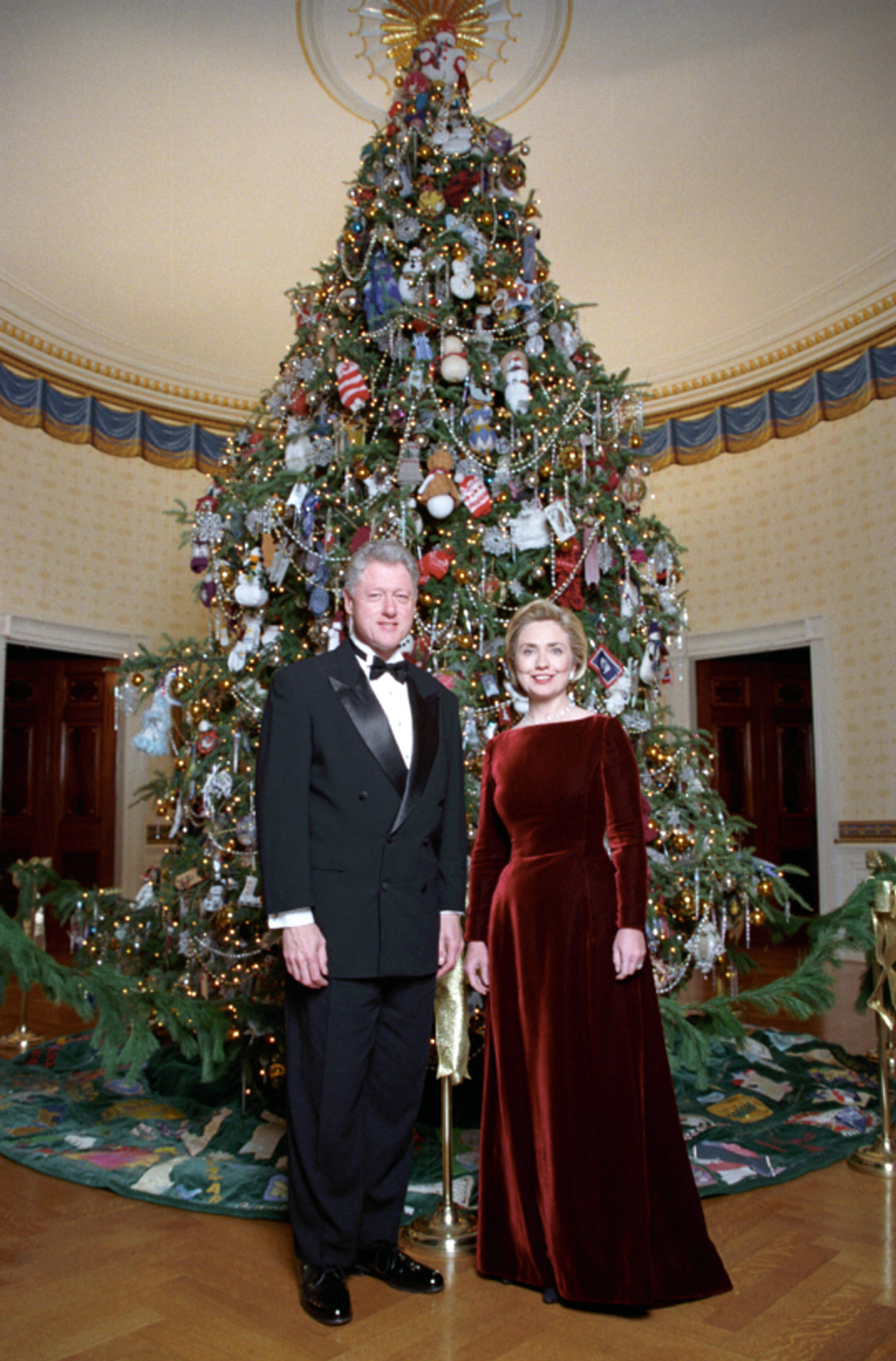 President Clinton and Hillary Rodham Clinton wear formal wear and pose next to the 1998 White House Christmas tree