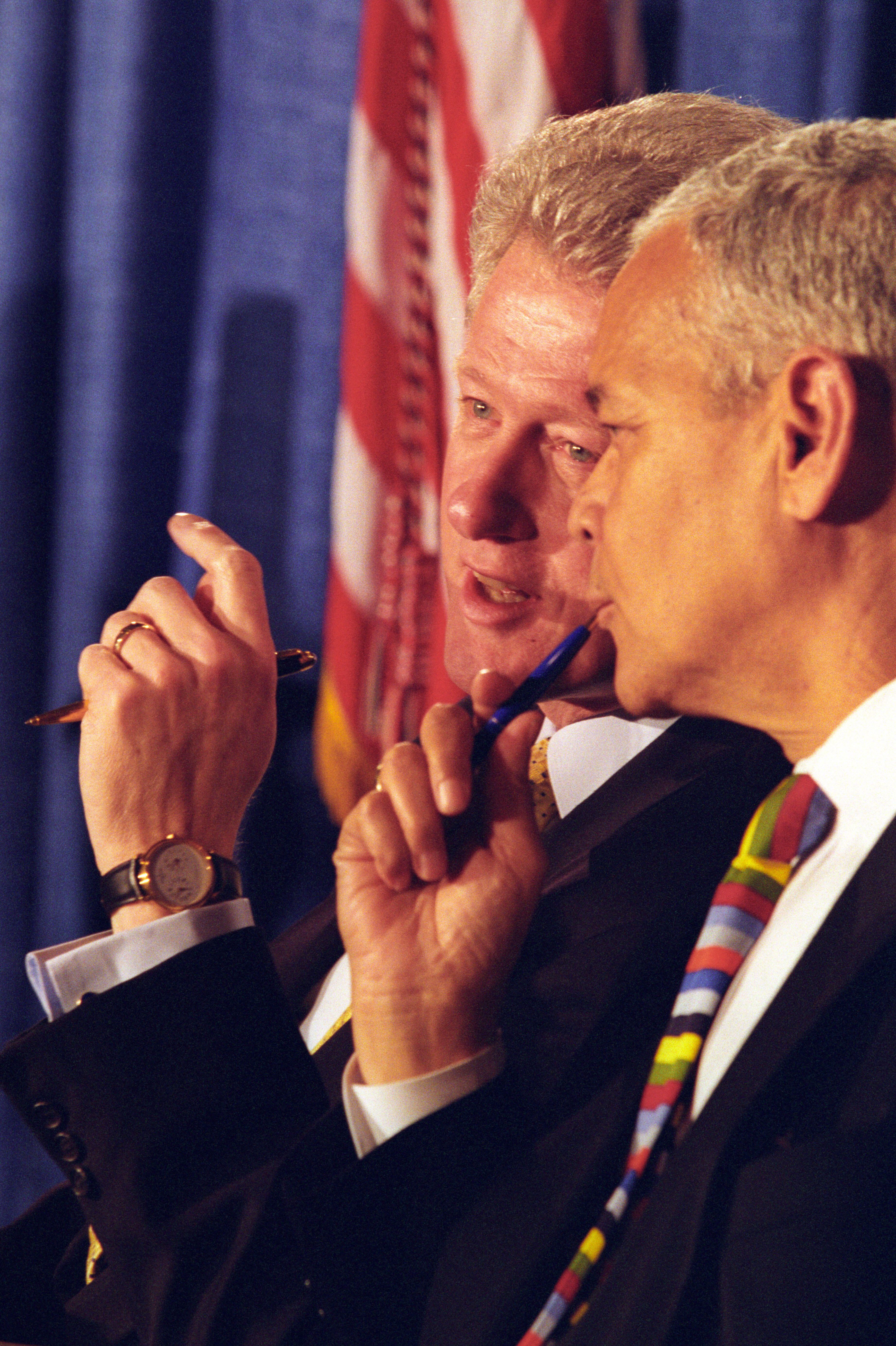 President Clinton sits next to President of the NAACP, Julian Bond. Both men are  speaking with each other. 