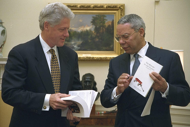 Gen. Colin Powell presents President Clinton with "The Report to the Nation." Both men stand. President Clinton flips through the bound report. Gen. Powell holds a copy of the bound report.