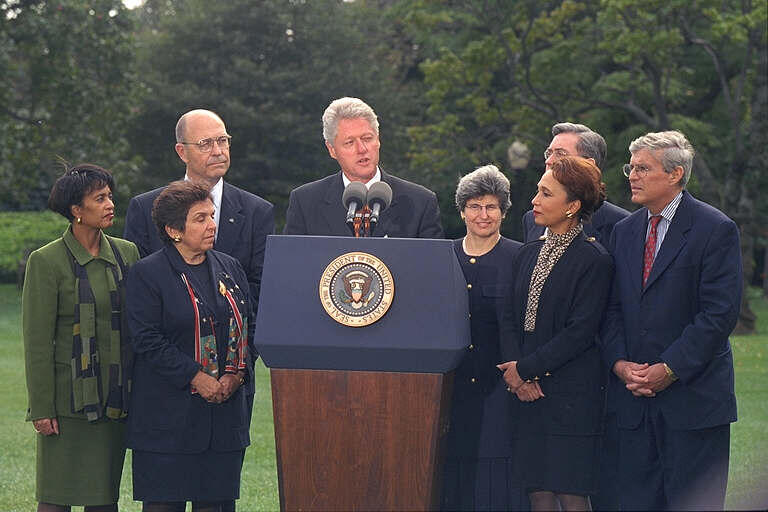 President Clinton stands behind a podium with Donna Shalala, Alexis Herman, Dr. Thomas Reardon, Beverly Malone, Judy Lichtman, John Seffrin, and Ron Pollack