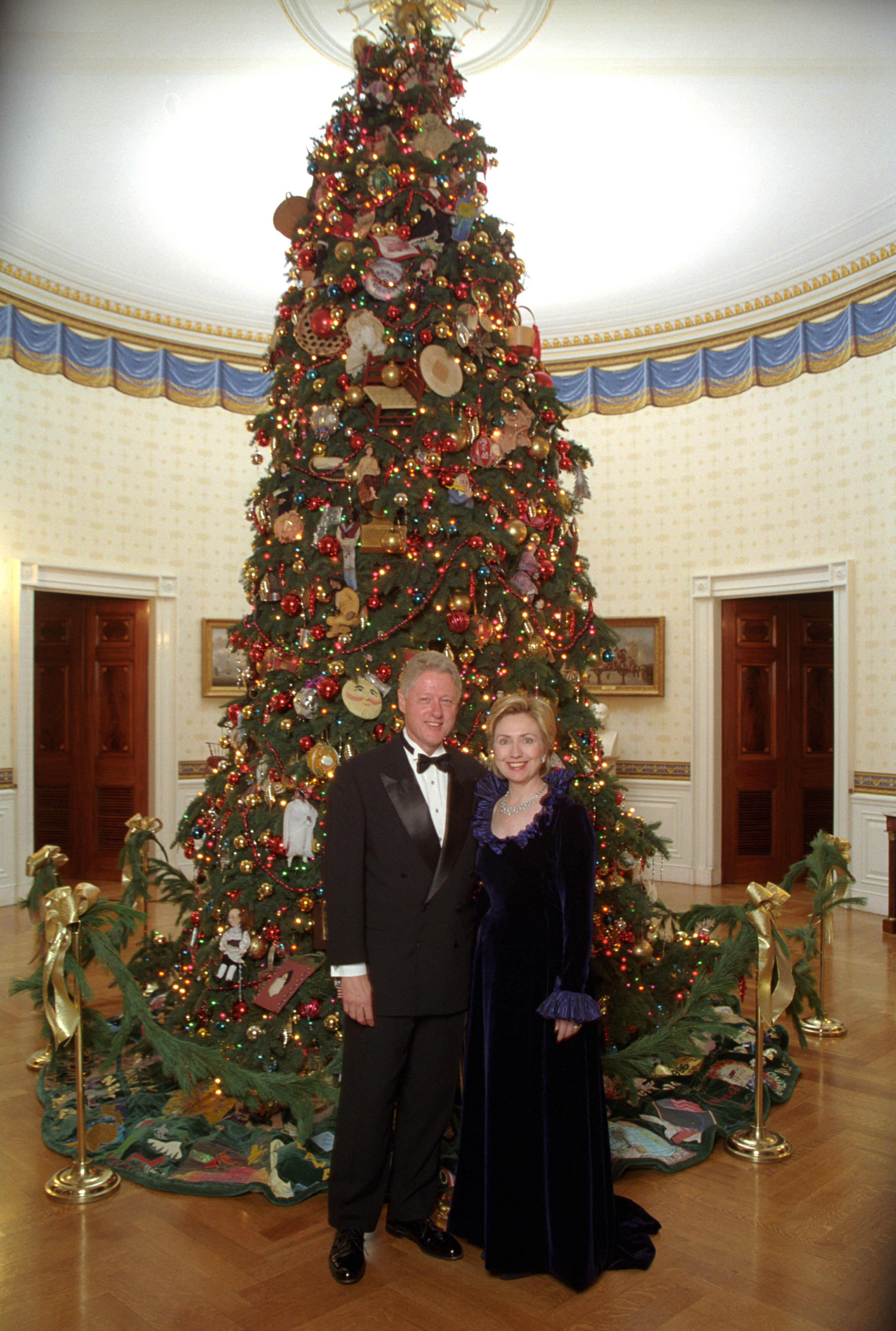 President Clinton and Hillary Rodham Clinton posing next to the 1999 White House Christmas tree for their official Christmas portrait