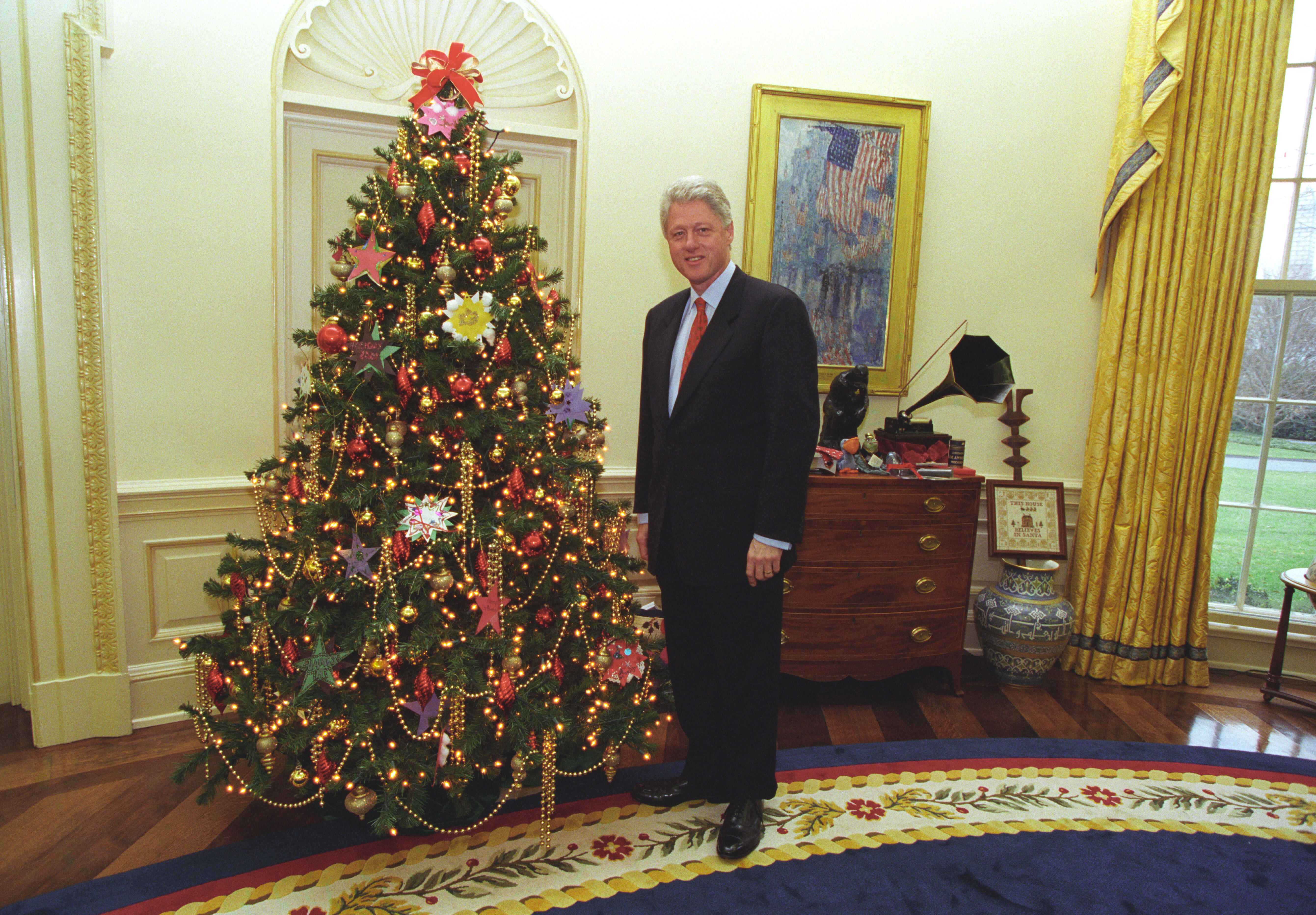 President Clinton stands and poses for a photograph next to the Christmas tree in the Oval Office