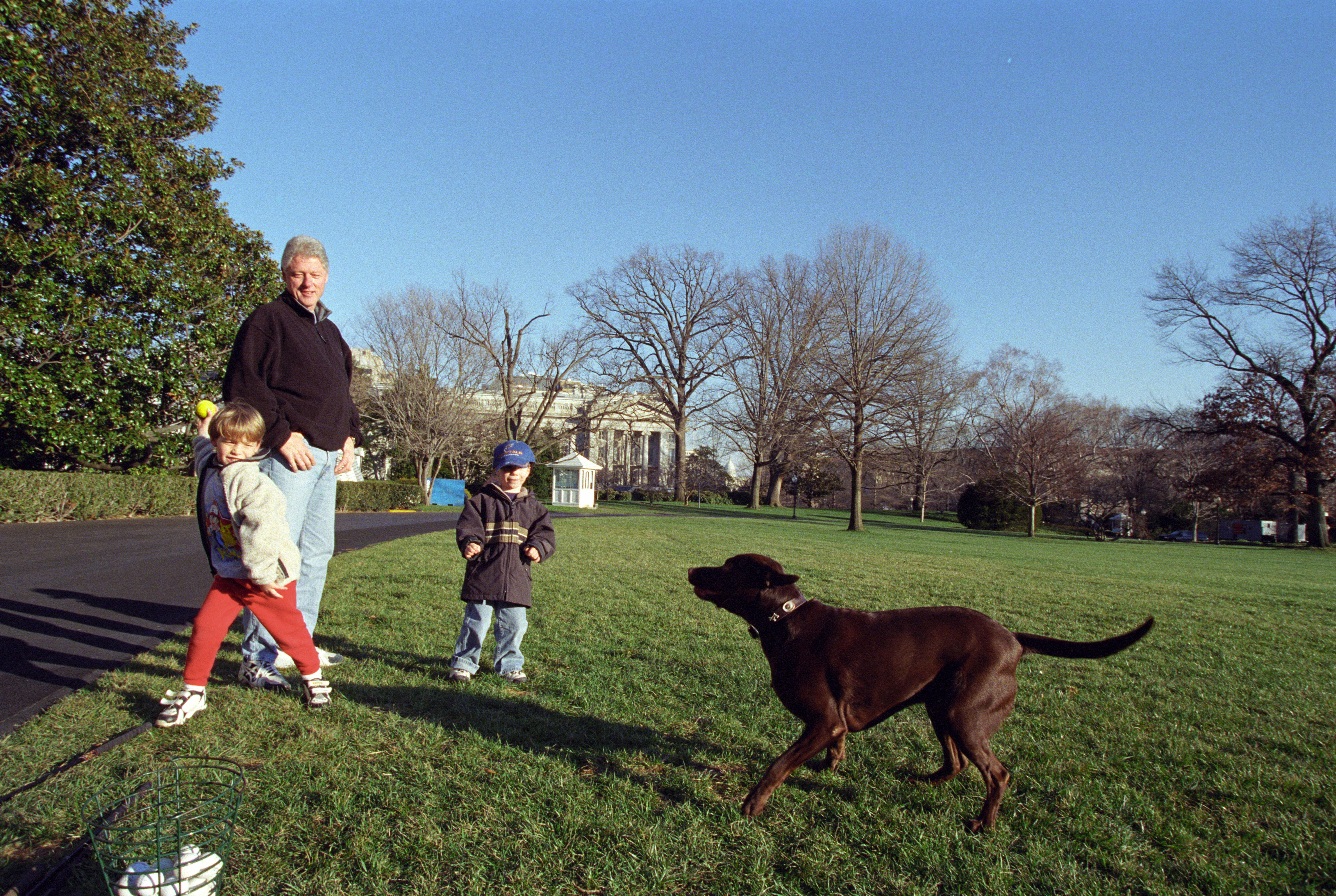 President Clinton and his young nephews, Tyler Cassidy Clinton, and Zach Rodham throw a ball to Buddy the brown Labrador dog on the South Lawn of the White House