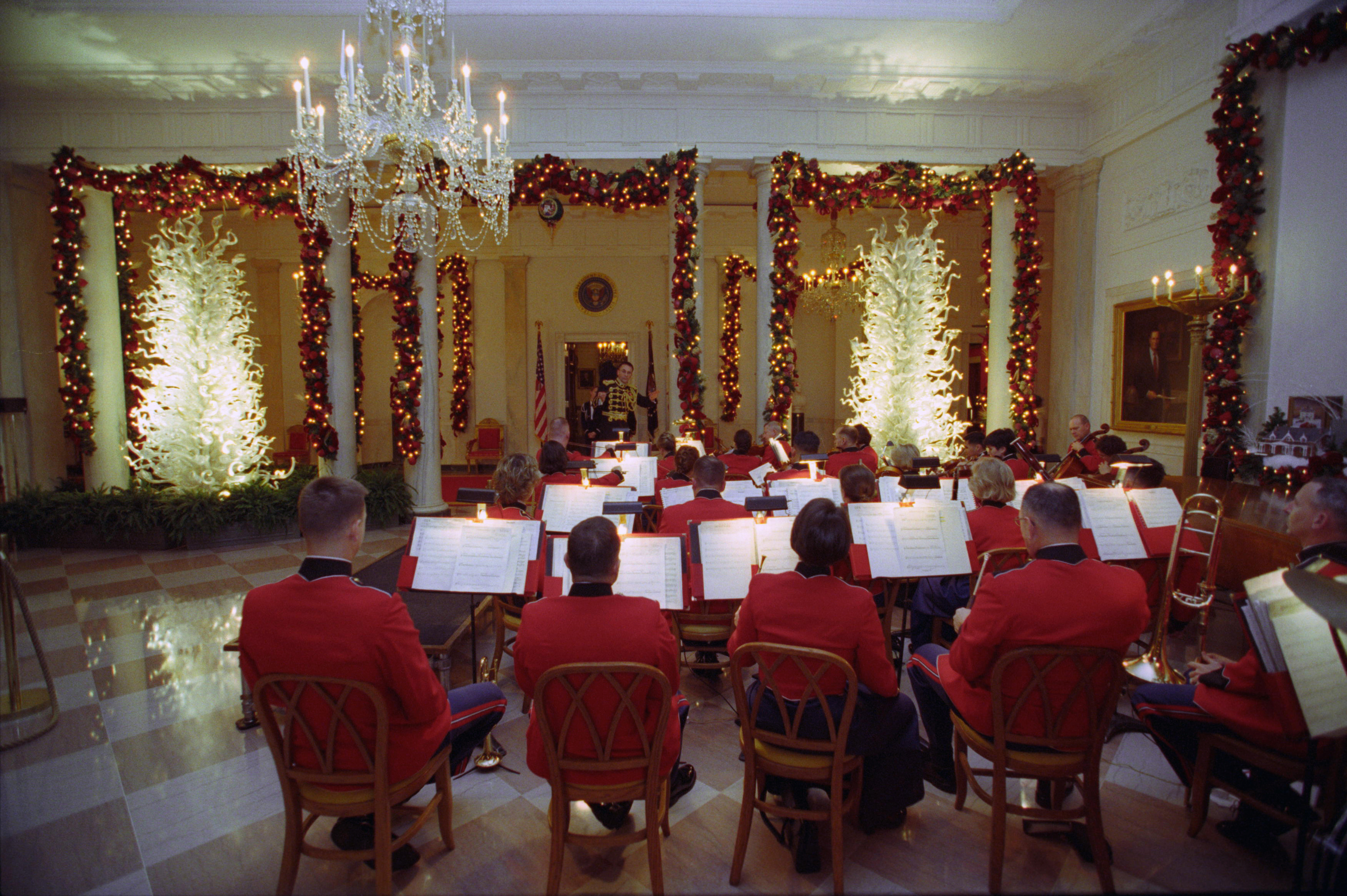 Marine Orchestra members face away from the camera, toward music stands. The music stands hold sheet music.