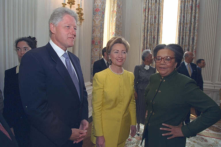 President Clinton and Hillary Rodham Clinton stand the White House State Dining Room with the founder of the Children's Defense Fund, Marian Wright Edelman. Edelman stands with her left arm bent, and her left hand on her hip. Five people can be seen in the background of the photograph.