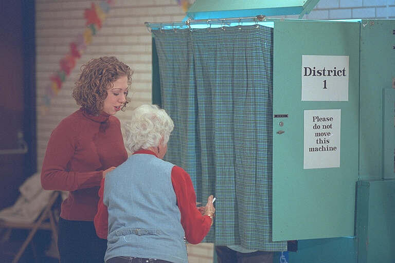 Chelsea Clinton is assisted by a poll worker outside of a voting machine. The  voting machine is aqua in color.