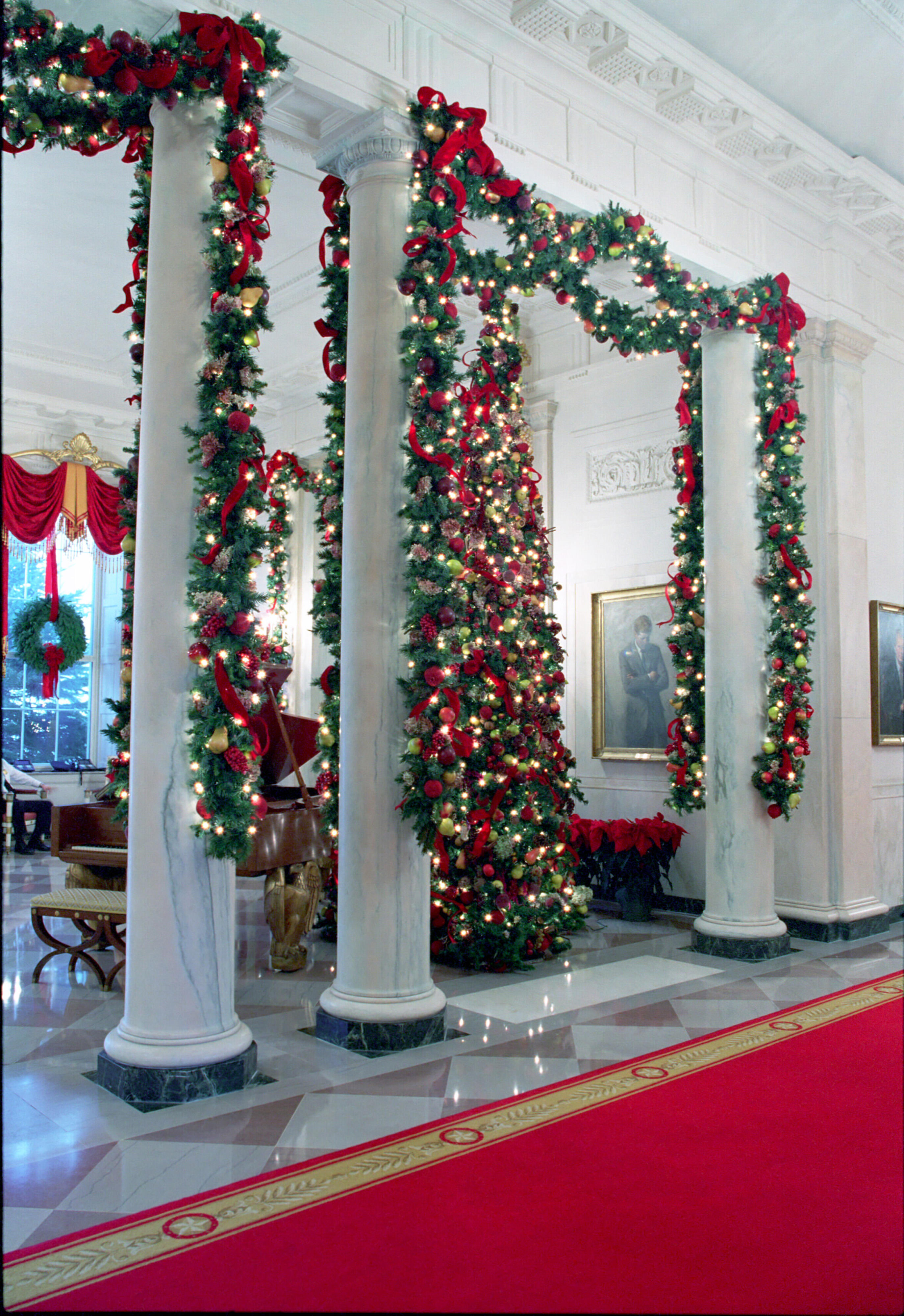 White columns covered in lighted garland with red bows. A lit Christmas tree can also be seen in the photograph.